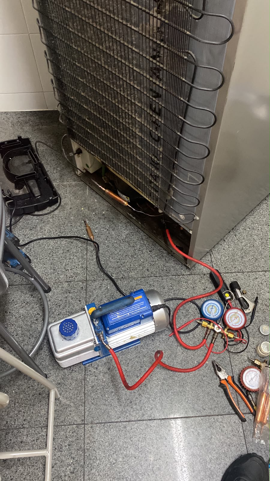 Parte traseira de equipamento de refrigeração durante manutenção com bomba de vácuo e manifold